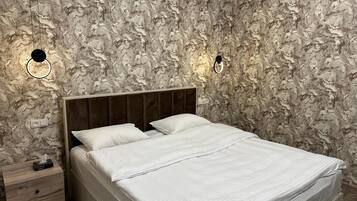 A bedroom with a marble-patterned wall, a wooden headboard, a bed with white bedding, and two wall-mounted light fixtures.
