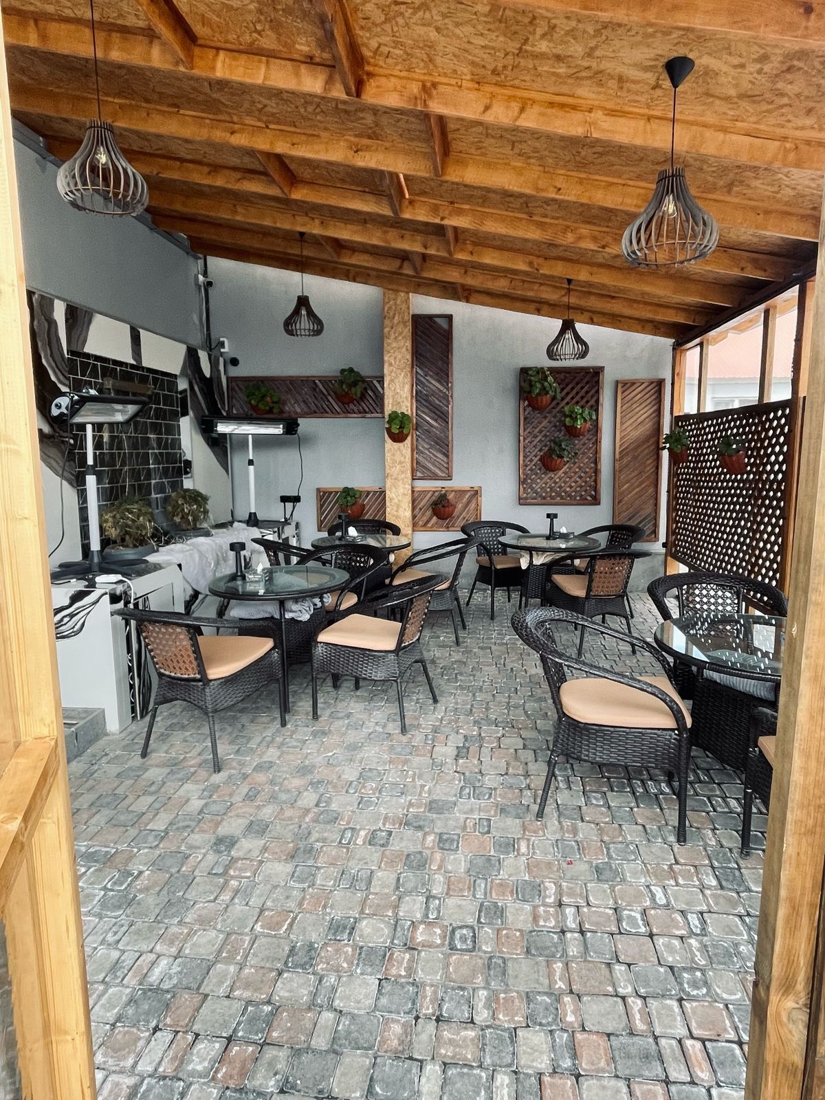 An outdoor patio area with stone flooring, wicker furniture, and hanging pendant lights.