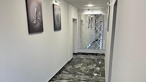 Ένας διάδρομος με μαρμάρινο δάπεδο, λευκούς τοίχους και τρία έργα τέχνης σε κορνίζες.