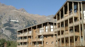 Un immeuble en bois à plusieurs étages, doté de balcons, qui se dresse sur un fond de paysage montagneux.
