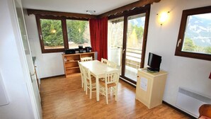 Une pièce chaleureuse avec une table à manger en bois, des chaises, un petit téléviseur posé sur un meuble et un radiateur.
