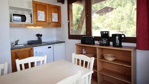Une cuisine compacte équipée d’un micro-ondes, d’un grille-pain et d’une machine à café sur le plan de travail, de placards en bois et d’une fenêtre donnant sur une maison et des arbres.