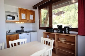 A compact kitchen with a microwave, toaster, and coffee maker on the counter, wooden cabinets, and a window with a view of a house and trees.