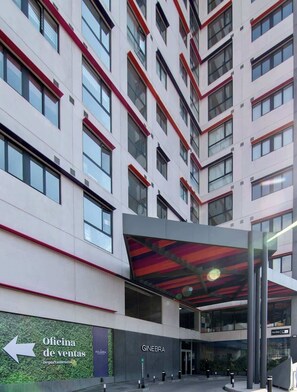 A multi-story building with a modern architectural design, featuring a prominent entrance with a glass facade and a red and black striped awning.