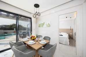 A dining area with a wooden table set for four, surrounded by grey chairs. A fruit bowl and a bottle are on the table.