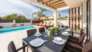Un área de comedor al aire libre con piscina, sillones de descanso y una mesa lista para una comida.