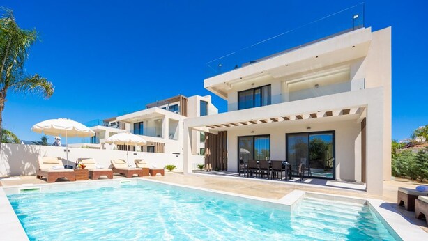 Una casa moderna con piscina, mobiliario exterior y cielo azul despejado.