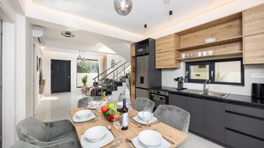 Una cocina moderna con comedor, que presenta una mesa de madera dispuesta para cuatro personas, un horno empotrado y un ventanal con vistas al jardín.
