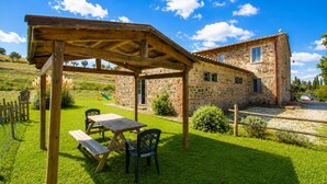 Une maison en pierre avec une pergola en bois et une table de pique-nique dans la cour.
