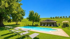 Une piscine avec des chaises longues, un bâtiment en pierre et un paysage verdoyant.