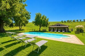 Una piscina con sillones de descanso, un edificio de piedra y un paisaje cubierto de césped.