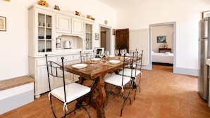 Une cuisine avec une table et des chaises en bois, des placards blancs et un sol carrelé.