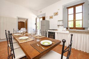 Un comedor con una mesa de madera dispuesta para cuatro, sillas y una cocina al fondo.