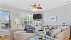 A modern living room with a sofa, armchairs, a coffee table, and a ceiling fan.