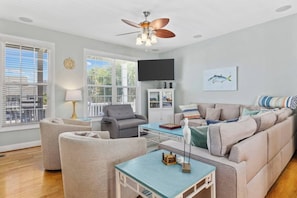 A modern living room with a sofa, armchairs, a coffee table, and a ceiling fan.