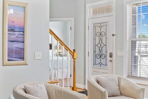 Una habitación con una escalera, una puerta con detalles de metal ornamental y dos sillones.
