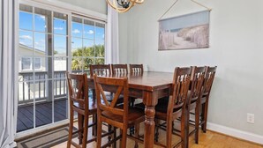 A dining area with a wooden table and chairs, a chandelier, and a view through large windows.