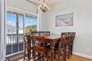 A dining area with a wooden table and chairs, a chandelier, and a view through large windows.