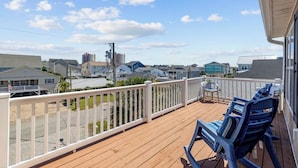 A wooden deck with a white railing, two blue chairs, and a view of a residential area with houses and a clear sky.