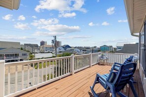A wooden deck with a white railing, two blue chairs, and a view of a residential area with houses and a clear sky.