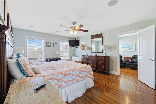 A bedroom with a bed, dresser, ceiling fan, and a door leading to another room.