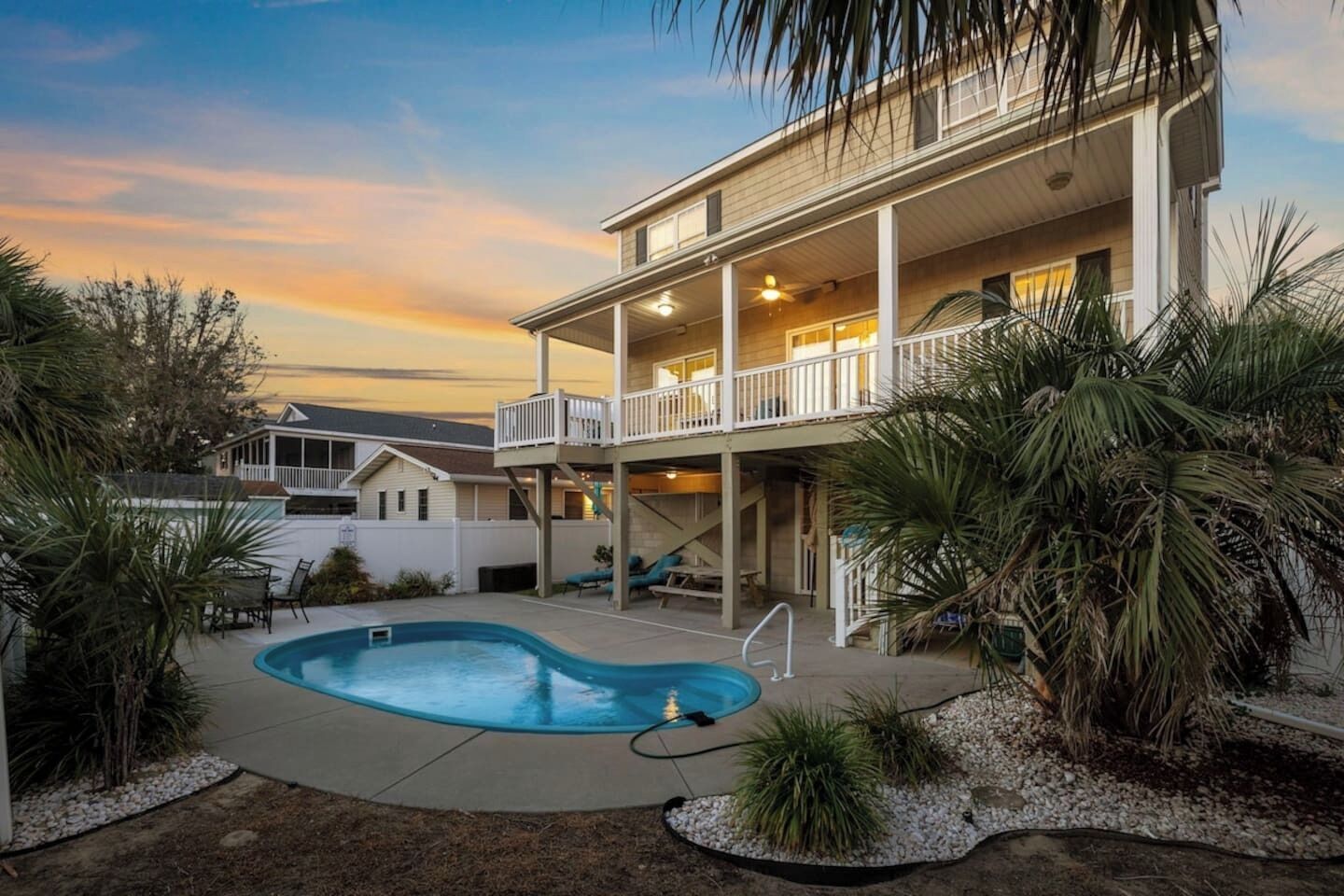A two-story house with a swimming pool, a covered patio, and a view of the sunset.