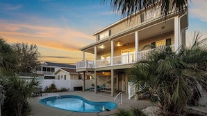A two-story house with a swimming pool, a covered patio, and a view of the sunset.