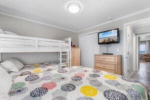 Une chambre avec des lits superposés, une télévision, une commode et une porte donnant sur une autre pièce.