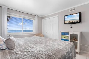 Un dormitorio con cama, televisor montado en la pared, ventana con persianas y armario.