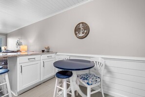 Une cuisine avec des meubles blancs, une table ronde bleue et une chaise blanche avec un coussin bleu.