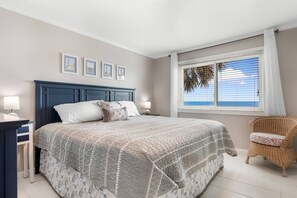 A bedroom with a large bed, a nightstand, a chair, and a window with a view.