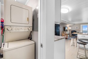 A laundry room with a washing machine and dryer, a kitchen area with a dining table and bar stools, and a view of the outside through a window.