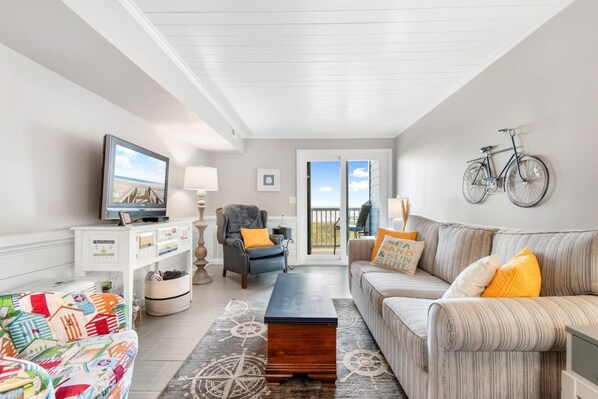 A living room with a television, sofa, armchair, and a view to the outside.