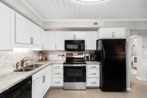 Una cocina moderna con armarios blancos, un refrigerador negro, electrodomésticos de acero inoxidable y un salpicadero de azulejos.