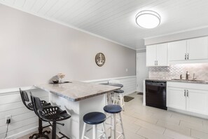 A kitchen with white cabinets, a marble countertop, a dishwasher, and a bar stool.