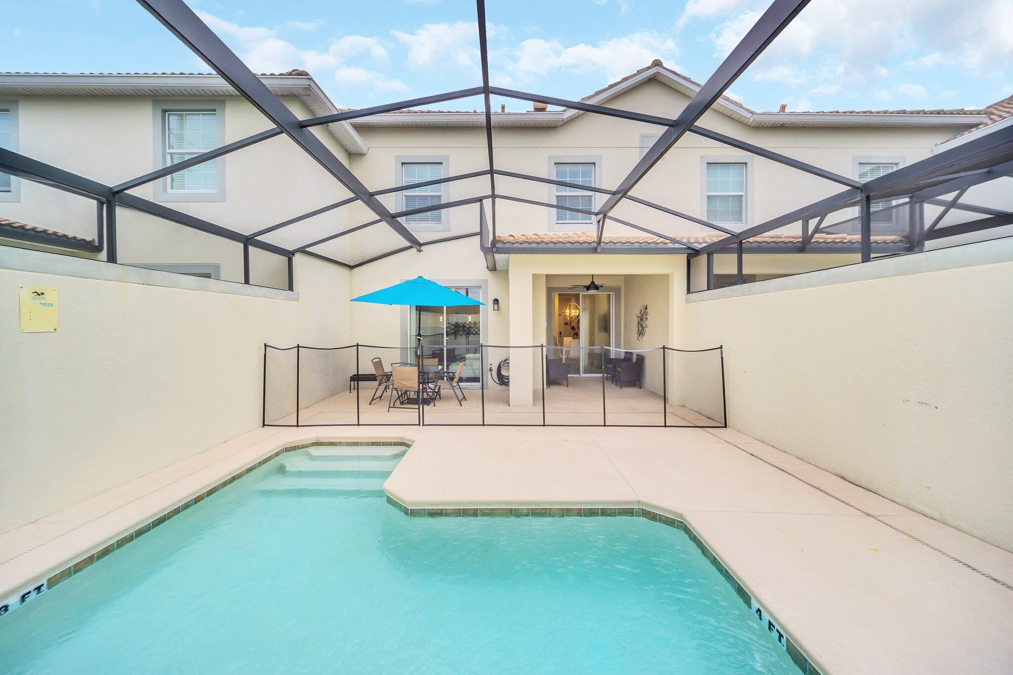 A swimming pool with a glass enclosure, a blue umbrella, and a view of a building with a tiled roof.