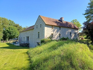 A stone house with a red-tiled roof, surrounded by lush greenery and a clear blue sky.