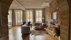 A spacious living area with a stone archway, wooden flooring, a sofa, a coffee table, and a TV mounted on a stone wall. - The panorama (Lyon)