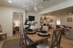 Un coin repas avec une table en bois, dressée pour quatre personnes, entourée de chaises. Un vase rempli de fleurs est posé sur la table, et un luminaire est suspendu au plafond.