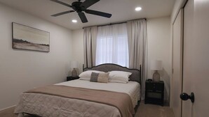 Une chambre à coucher avec un lit, un ventilateur de plafond, une table de chevet avec une lampe et une porte.