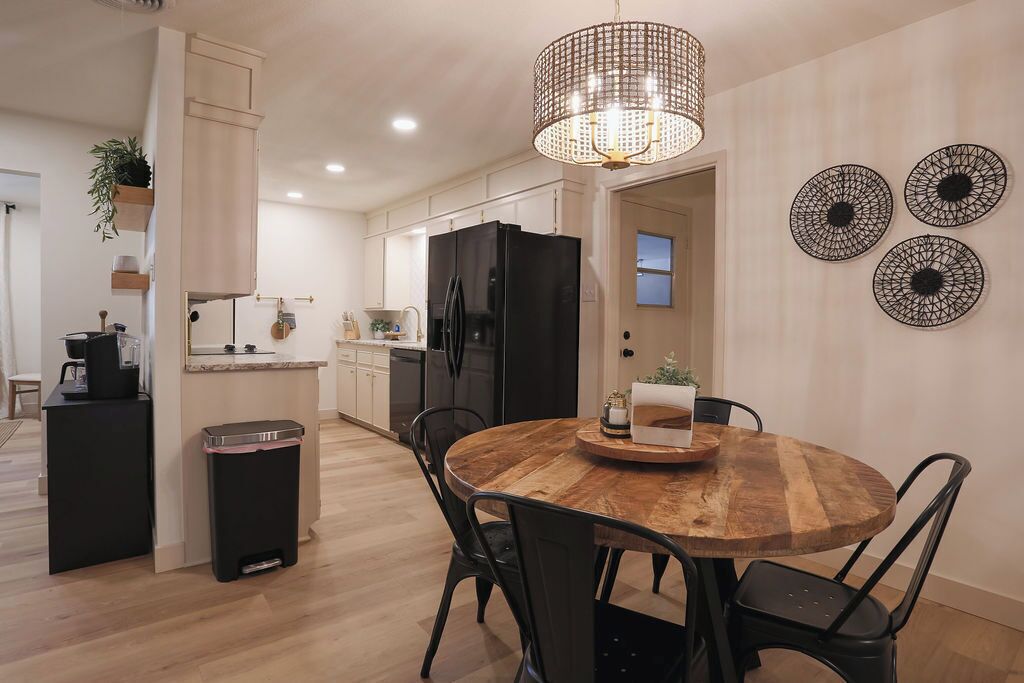 Una cucina moderna con frigorifero nero, tavolo da pranzo in legno e sedie nere. Si nota un cestino e una pianta pensile.