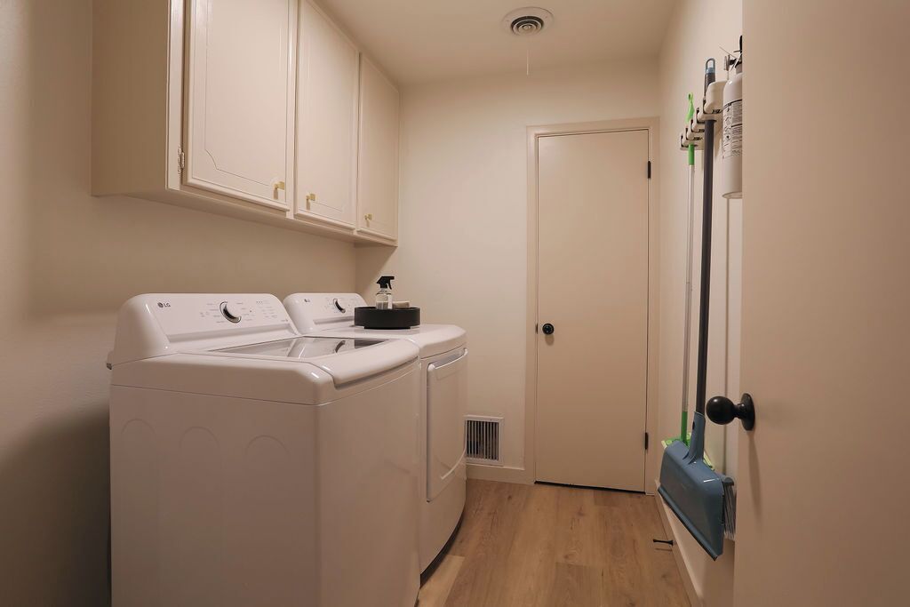 A laundry room with a front-loading washer and dryer, a door, and a mop leaning against the wall.