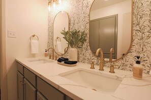 Une salle de bain avec deux lavabos, des robinets dorés, un grand miroir et une plante en pot.