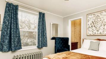 Un dormitorio con una cama grande, un radiador, una silla y una ventana con cortinas.