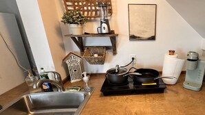 Une cuisine équipée d’un évier en acier inoxydable, d’un plan de travail en bois, d’une cuisinière électrique noire, d’un mixeur et d’une machine à café.
