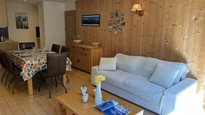 A modern living room with a wooden wall, a light blue sofa, a dining table with chairs, and a wooden coffee table.