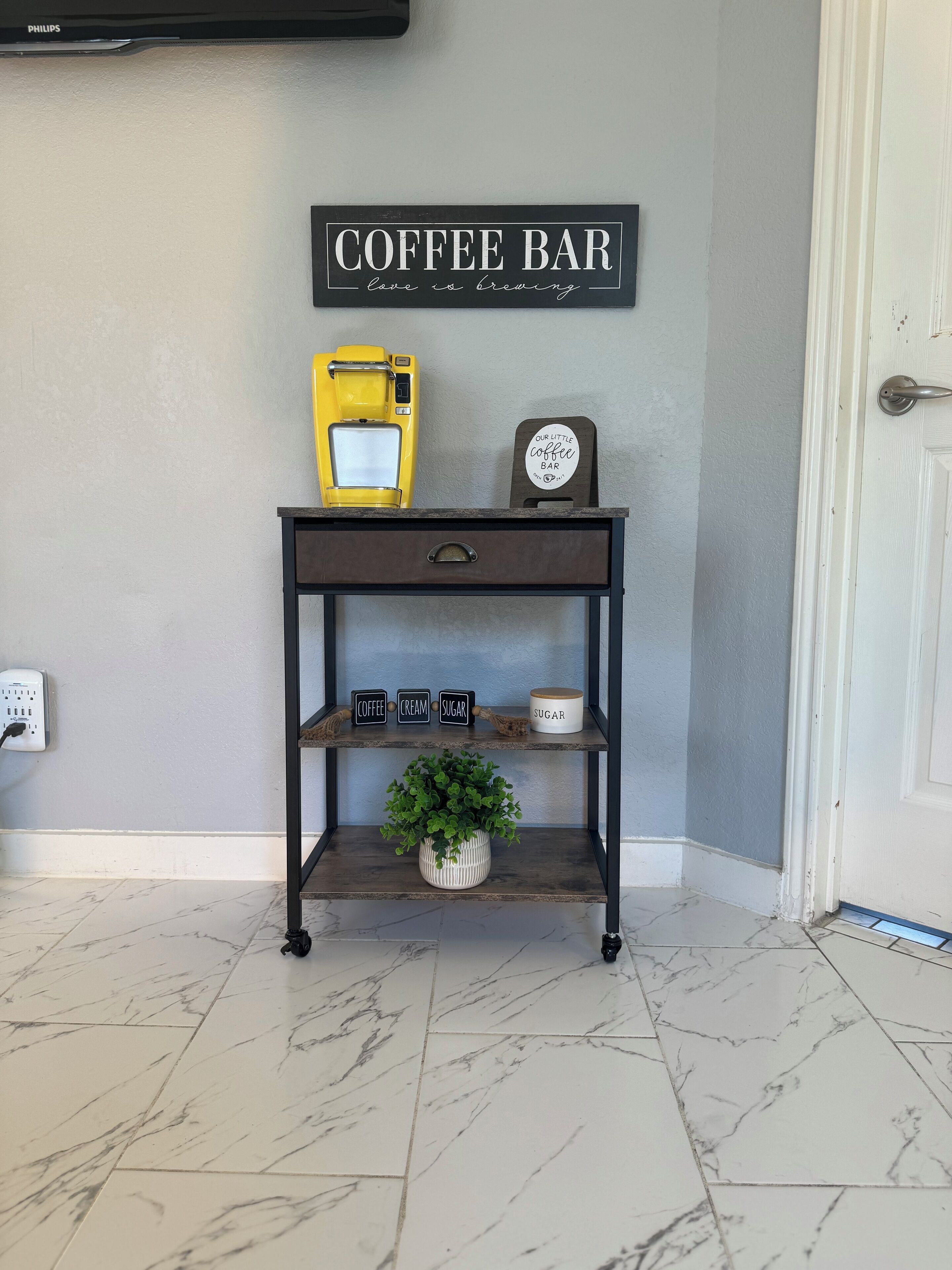Een koffiebar met een koffieapparaat, een bord waarop 'COFFEE BAR' staat en een plank met gelabelde bakken voor koffie, room en suiker.