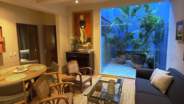A living room with a dining area, a sofa, and a glass door leading to a garden with plants. - Parque Juan Diego (Zapopan)