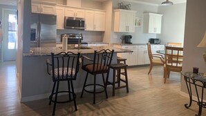 A modern kitchen with white cabinets, stainless steel appliances, and a central island with chairs. - Sunsets over Siesta Key in this cozy 2+2 condo
 (Sarasota)