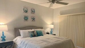 A bedroom with a bed, two bedside tables, a ceiling fan, and a window with blinds. - Sunsets over Siesta Key in this cozy 2+2 condo
 (Sarasota)